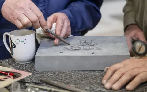 Kamieniarz z kubkiem "Pete" rzeźbi w kamieniu. Zastanawiasz się, ile zarabia kamieniarz? To zależy od doświadczenia i umiejętności.