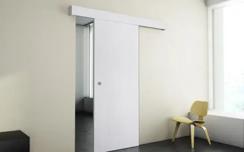 Puerta corredera blanca moderna instalada en pared beige, con silla amarilla y ventana al fondo.