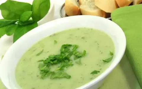 Un bol de soupe à l'oseille crémeuse, garnie d'herbes fraîches, avec du pain en arrière-plan.