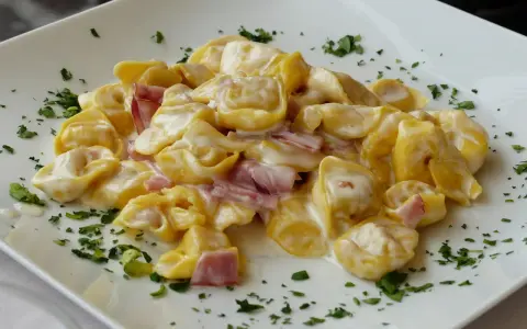 Tortellini panna e prosciutto, un piatto cremoso e saporito, guarnito con prezzemolo fresco su un piatto bianco.