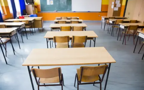 Pusta klasa szkolna z rzędami ławek i krzeseł. W tle tablica i okna. Obowiązek nauki czeka na uczniów.