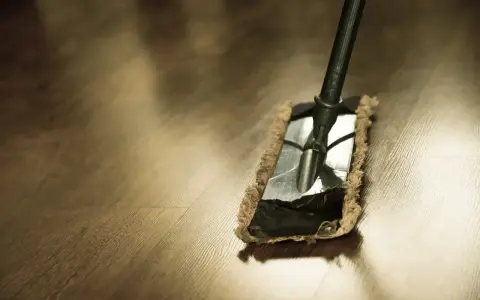 Mop usuwa tłustą plamę po wosku z drewnianej podłogi.