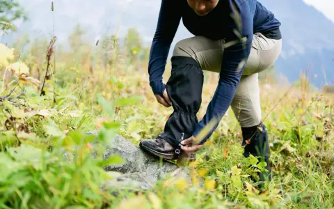Une personne ajuste ses guetres de randonnée dans un paysage naturel.