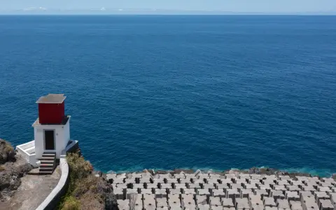 Kleines rotes Haus auf Felsen am Meer bei Ribeira Brava. Wellenbrecher aus Beton säumen die Küste.