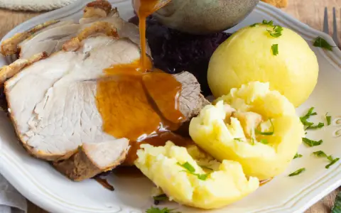 Omas Sonntagsessen: Saftiger Schweinebraten mit knuspriger Kruste, Klößen und Rotkohl, übergossen mit dunkler Soße.