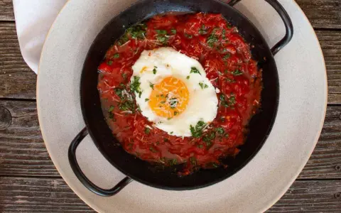 Ein Spiegelei ruht in einer würzigen Tomatensoße, garniert mit Kräutern und Käse. Ein Gericht, das an "uova in purgatorio" erinnert.