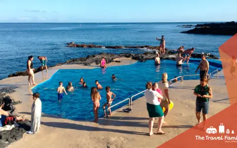 Famiglia felice alle Azzorre con bambini che nuotano in una piscina naturale.