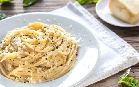 Piatto di pici cacio e pepe, conditi con abbondante pecorino e pepe nero macinato fresco, su un tavolo di legno rustico.