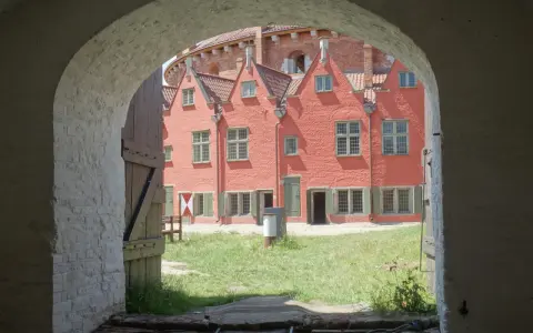 Przez łuk widać dziedziniec twierdzy Wisłoujście z ceglanymi budynkami i zieloną trawą.