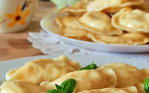 Słowackie pierogi z bryndzą na talerzu, ozdobione listkami bazylii.
