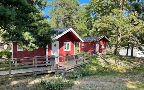 Röda stugor med träaltaner och ramper på Waxholms camping, omgivna av grönska och träd.