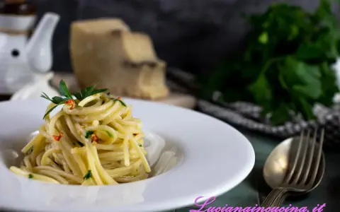 Un piatto di spaghetti alla carrettiera, conditi con aglio, olio, peperoncino e prezzemolo, con pecorino grattugiato sullo sfondo.