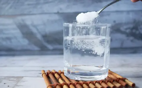 Salz und Zucker werden in ein Glas Wasser gegeben, um Elektrolyte selber machen.
