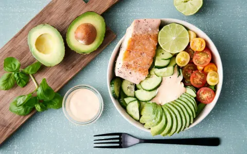 En hälsosam keto recept-bowl med lax, avokado, gurka, tomater och en krämig dressing.