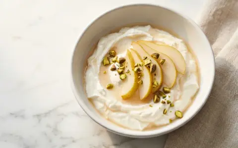 Cremiger Joghurt, der zu lange im Joghurtbereiter war, serviert mit Birnenspalten, Honig und gehackten Pistazien.