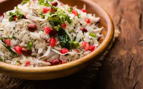 Salade de riz gastronomique, un plat coloré avec des grains de grenade, des cacahuètes et de la coriandre fraîche dans un bol en bois.