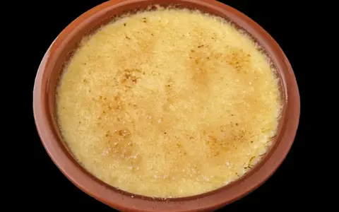 Crème brûlée dans un ramequin en terre cuite, sa surface caramélisée craque sous la cuillère.