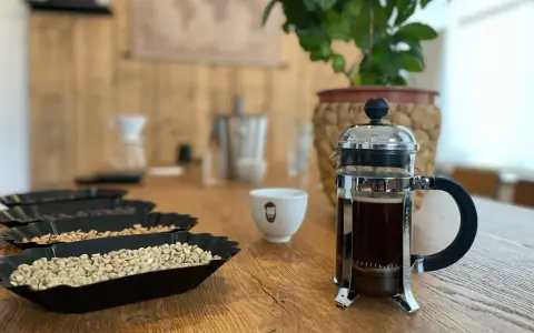 Eine French Press mit frisch gebrühtem Kaffee steht neben einer Tasse und Schalen mit Kaffeebohnen.