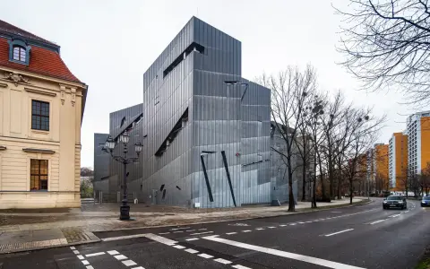 Nowoczesny budynek Muzeum Żydowskiego w Berlinie, obok zabytkowej kamienicy, z charakterystyczną, poszarpaną fasadą.