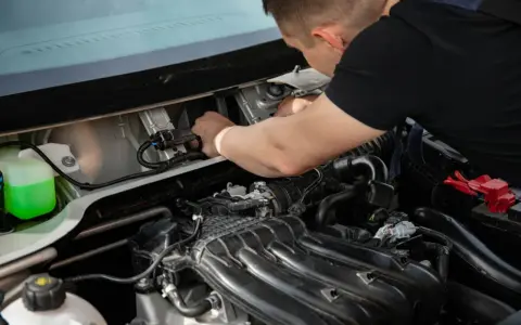 Mechanik naprawia silnik, prawdopodobnie usuwając uciążliwy błąd P0011. Widać zbiornik płynu i elementy silnika.