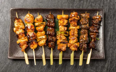 Różnorodne yakitori na talerzu: kurczak, warzywa i inne przysmaki, apetycznie wyglądające i gotowe do jedzenia.