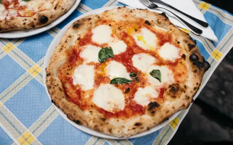 Pyszna pizza napolitana z pomidorami, mozzarellą i bazylią na niebieskim obrusie.