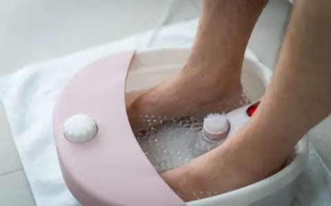 A person's feet are soaking in a foot spa machine filled with bubbly water. You can put water, bath salts, or essential oils in a foot spa machine for a relaxing experience.
