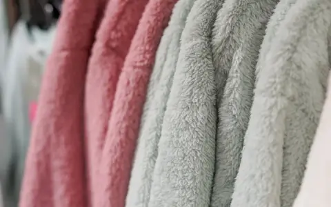 Des vêtements douillets en matière molleton, aux couleurs rose et vert d'eau, sont suspendus sur des cintres.