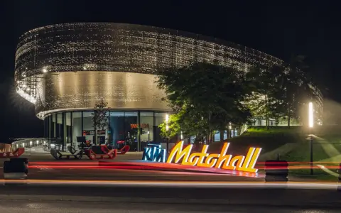 Insegna luminosa KTM Motohall di notte, con il moderno edificio illuminato e le scie luminose delle auto.