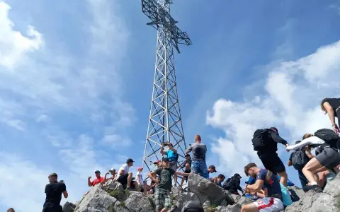 Grupa turystów na skalistym szczycie pod wieżą widokową w masywie górskim w Tatrach Zachodnich.