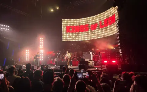 Koncert Kings of Leon na żywo. W tle wielki ekran z napisem "KINGS OF LEON", na scenie zespół gra dla rozentuzjazmowanej publiczności.