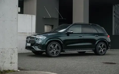 Ciemnozielony Mercedes GLE AMG stoi przed nowoczesnym budynkiem.