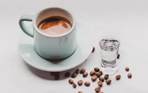 Kawa i alkohol skutki: filiżanka espresso obok kieliszka z wodą i rozsypane ziarna kawy.