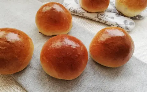 Pięć puszystych bułek maślanych, lśniących od pieczenia, ułożonych na lnianej serwetce. Idealne na śniadanie.