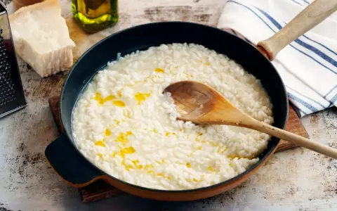 Krämig risotto i panna med en träsked. Bredvid syns parmesanost, olivolja och en rivare. Frågan är om man kan frysa risotto?