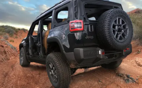 Un fuoristrada elettrico Jeep nero affronta un sentiero sterrato nel deserto, con le portiere aperte e una ruota di scorta sul retro.