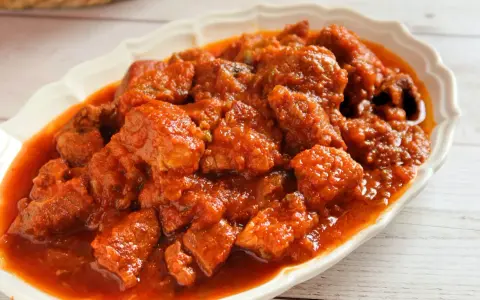Plato de magro con tomate, trozos de carne tierna en una salsa roja y sabrosa, servido en una fuente blanca.