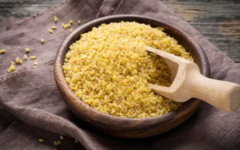 Holzschale mit Bulgur, bereit zum Bulgur kochen. Ein Holzschöpfer liegt darin.