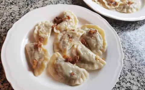 Pyszne pierogi z kapustą i grzybami, posypane skwarkami, na białym talerzu.
