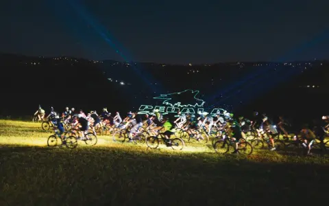 Ciclisti nella notte, illuminati da laser che formano il logo "Pedala coi Lupi". Un'avventura notturna su due ruote.