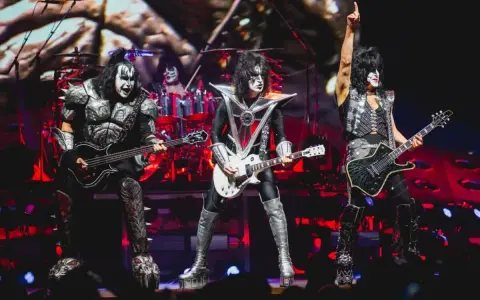 Les membres du groupe de rock Kiss, maquillés et costumés, jouent sur scène. Un chanteur lève un bras en signe de victoire.
