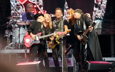 Medlemmar av E Street Band på scen, med Bruce Springsteen i mitten, omgiven av bandmedlemmar som spelar gitarr.
