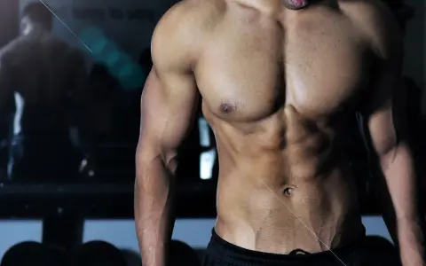 Muskulös man med synliga magmuskler i gym. En spegelbild av en annan person syns i bakgrunden. Frågan "hur deffar man" kan besvaras med denna fysik.