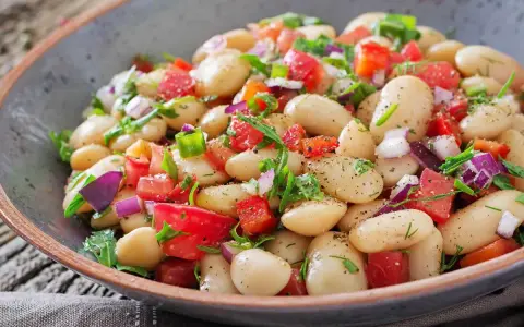 Un'insalata di fagioli sfiziosa, ricca di pomodori freschi, cipolla rossa e erbe aromatiche, servita in una ciotola rustica.