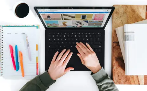 Hände tippen auf einem Laptop, daneben ein Kalender und eine Kaffeetasse.