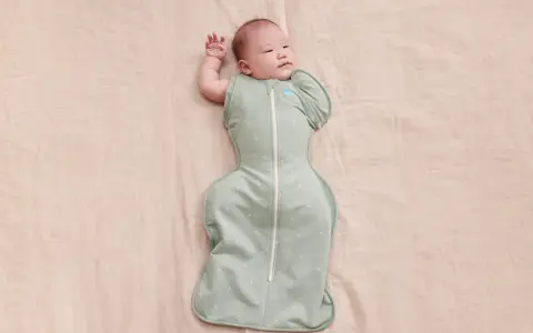Un neonato dorme sereno, avvolto in una fascia che lo culla dolcemente.