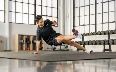 Un homme en tenue de sport exécute un exercice de planche latérale dans une salle de sport.