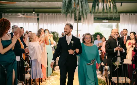 El novio sonriente camina del brazo de su madrina, ambos sonríen a los invitados.