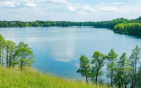Malownicze żnin jezioro otoczone zielenią, z widocznymi domami na horyzoncie i błękitnym niebem z chmurami.