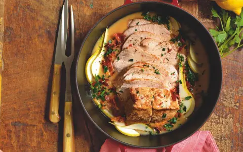 Lonza di maiale in padella morbida, affettata e servita con pere, salsa cremosa e prezzemolo tritato.